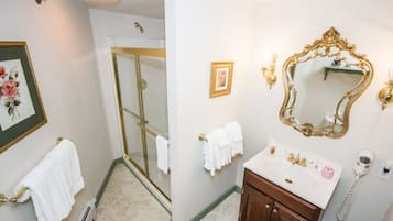 Um banheiro com chuveiro de vidro, toalhas brancas, um lavatório com pia e um espelho grande e decorativo.