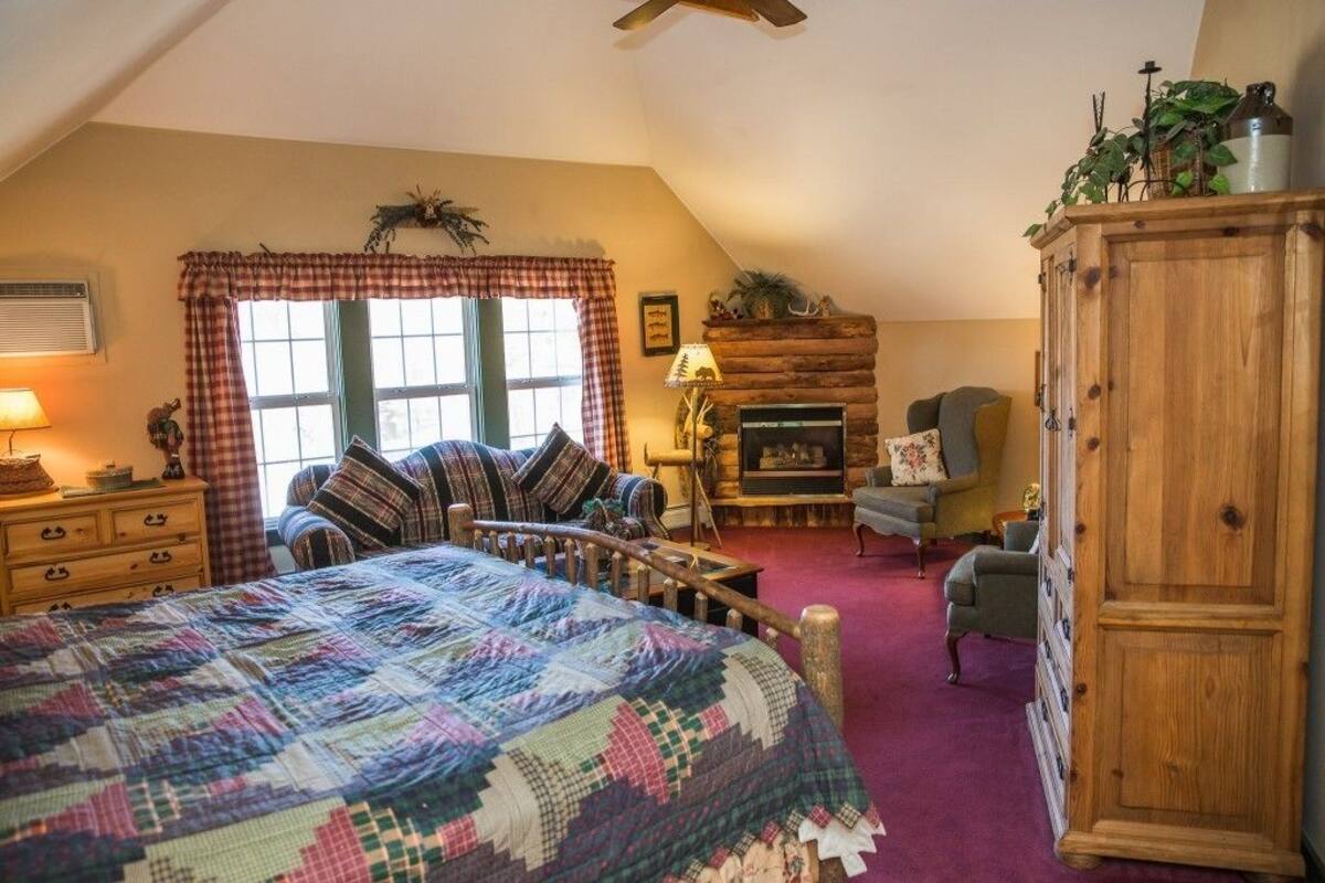 A cozy bedroom with a large bed, a fireplace, a wooden wardrobe, and a window with curtains.