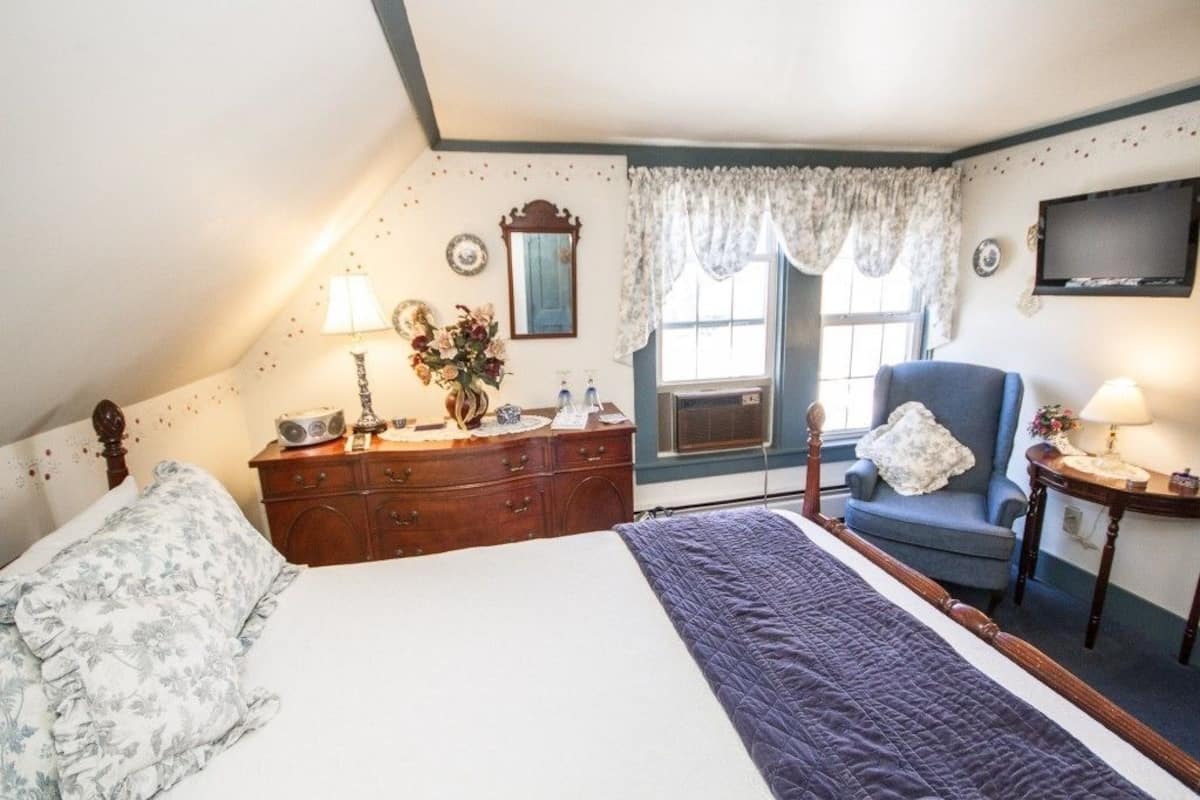 A bedroom with a bed, dresser, chair, and a television on the wall.