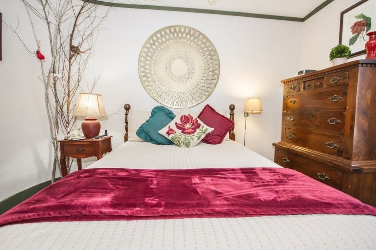 A bedroom with a bed, two nightstands, a dresser, a wall decoration, and a red blanket.