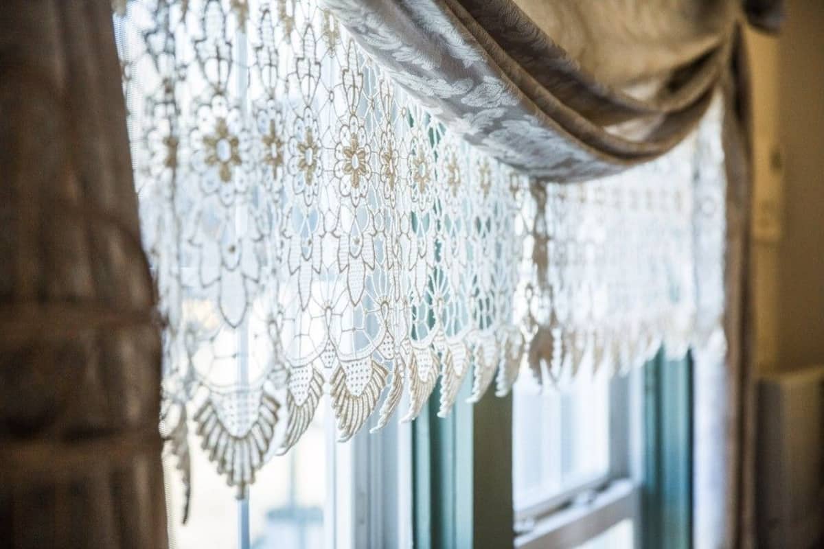 A window with a detailed lace curtain and a draped fabric.