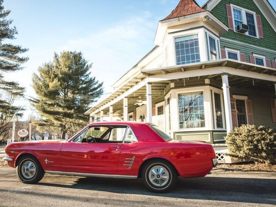 A red vintage car parked in front of a house with a green roof and white trim.