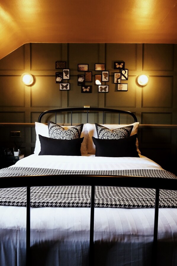 A neatly arranged bedroom with a bed centered in the room, flanked by wall-mounted light fixtures and framed artwork. - King William Rooms (Wilmslow)