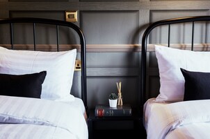 A hotel room with two beds, each with white bedding and black headboards. There is a small table between the beds with a book, a plant, and a decorative item.