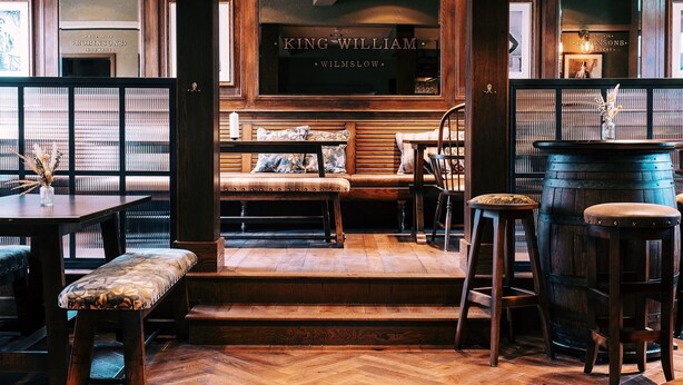 Un rincón de bar acogedor con muebles de madera, un barril grande y un letrero que dice 'King William Wilmslow'.