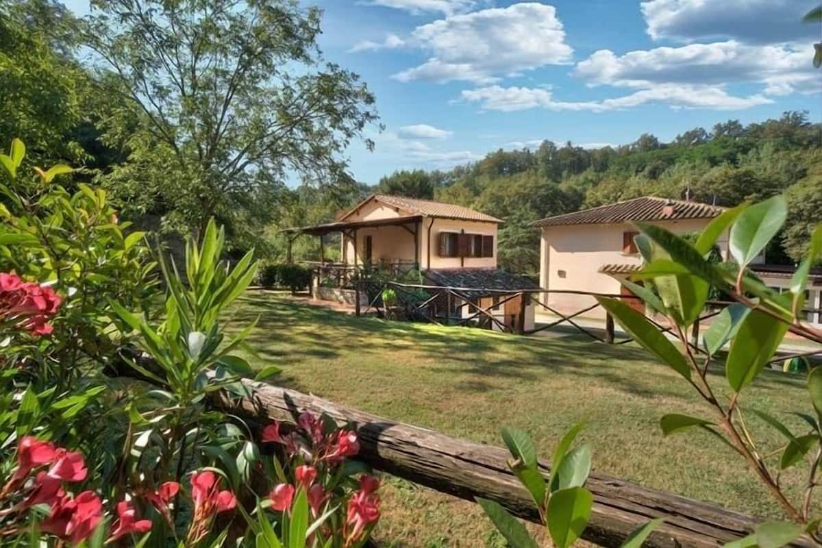 A rural setting with two small houses, surrounded by lush greenery and a clear sky.