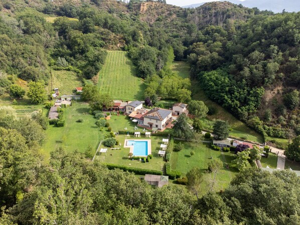 Vista aerea di una grande tenuta con diversi edifici, una piscina e ampi prati verdi.