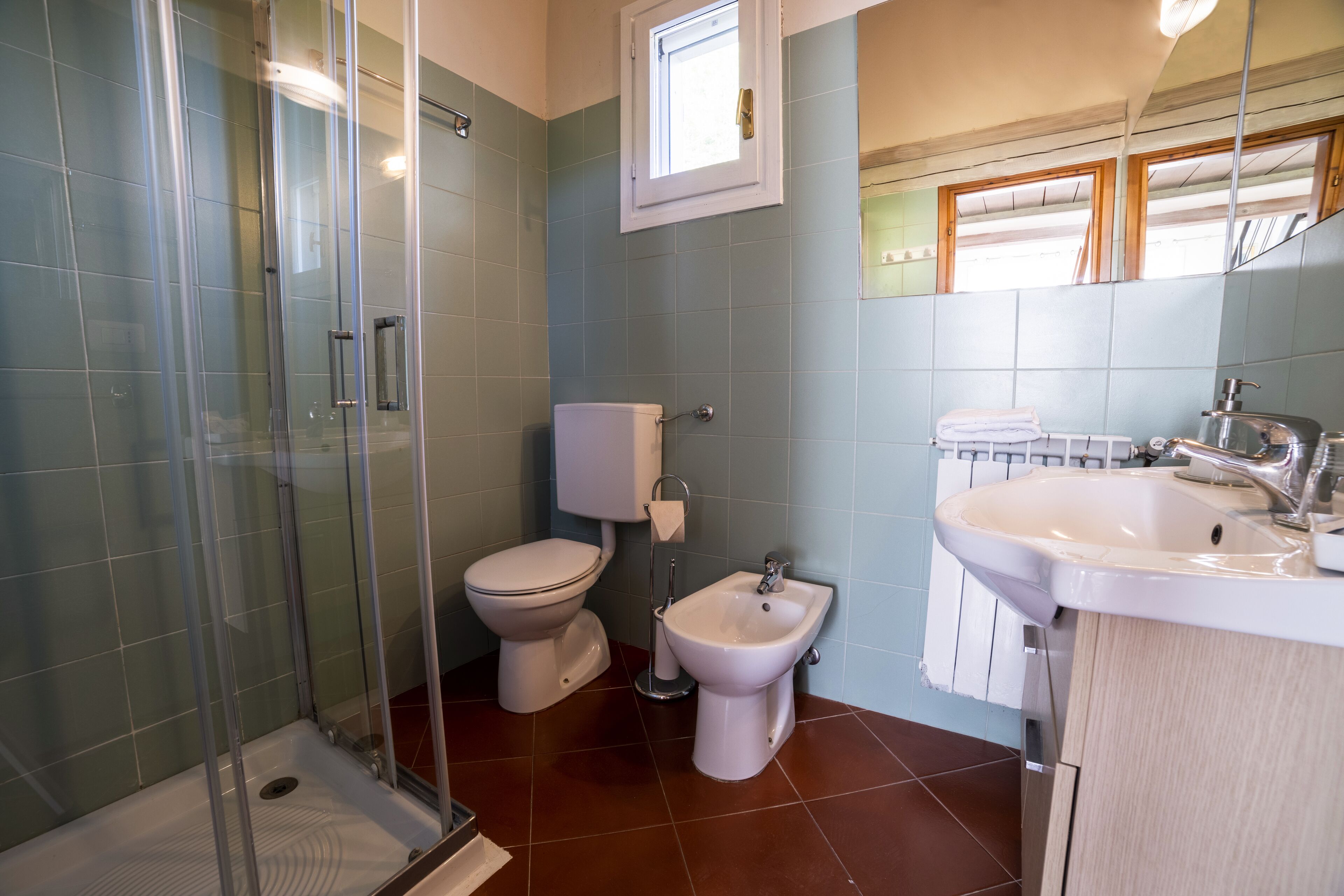 A modern bathroom with a glass-enclosed shower, a toilet, a bidet, and a sink.