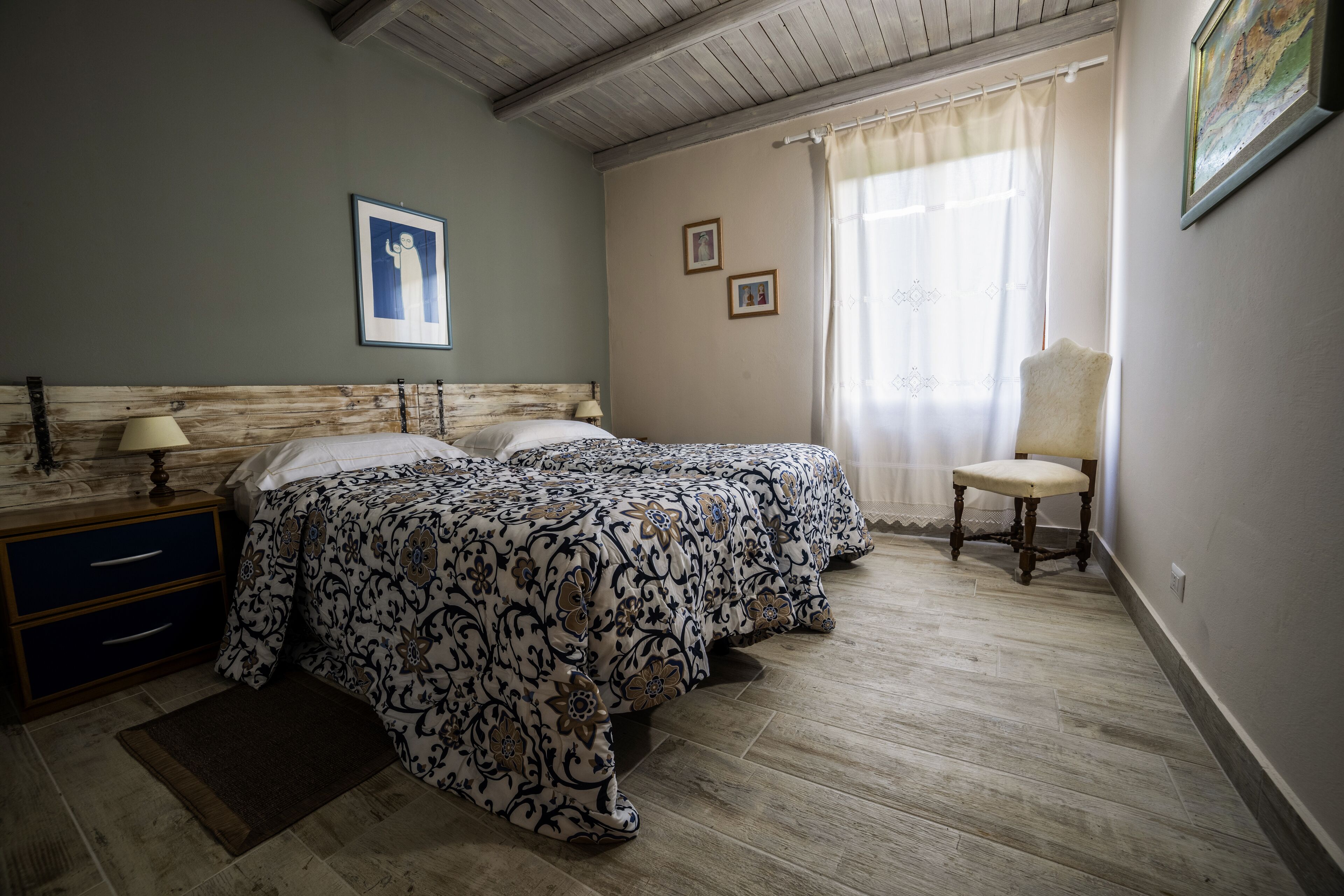 Un dormitorio con dos camas, una mesita de noche, una silla y una ventana con cortinas.