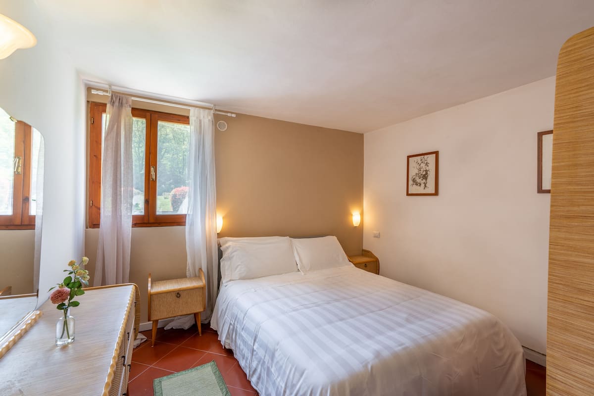 A bedroom with a bed, bedside tables, a desk, and a window with curtains.