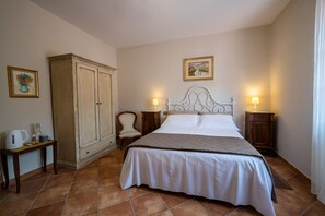 Una camera da letto con un letto, comodini, un armadio, una sedia e un tavolino con un bollitore e una bottiglia.