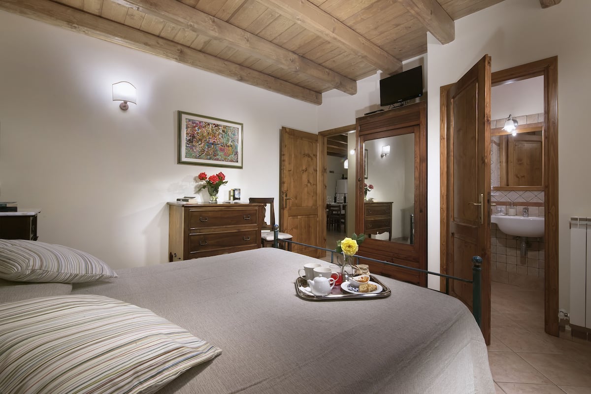 A bedroom with a bed, a tray with breakfast items, a painting, and wooden furniture.