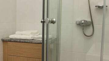 A glass-enclosed shower with a handheld showerhead and a wall-mounted faucet.