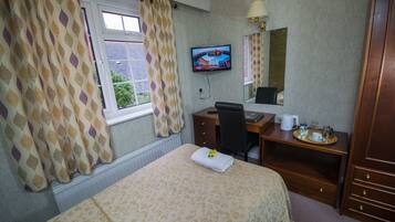 A hotel room with a bed, a desk, a chair, a television, and a window with curtains.