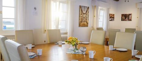 A dining room with a wooden table set for six, surrounded by six chairs, with a vase of flowers in the center.
