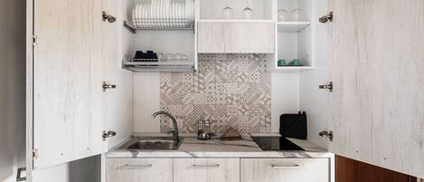 A compact kitchen with a built-in sink, white cabinets, and a patterned backsplash.