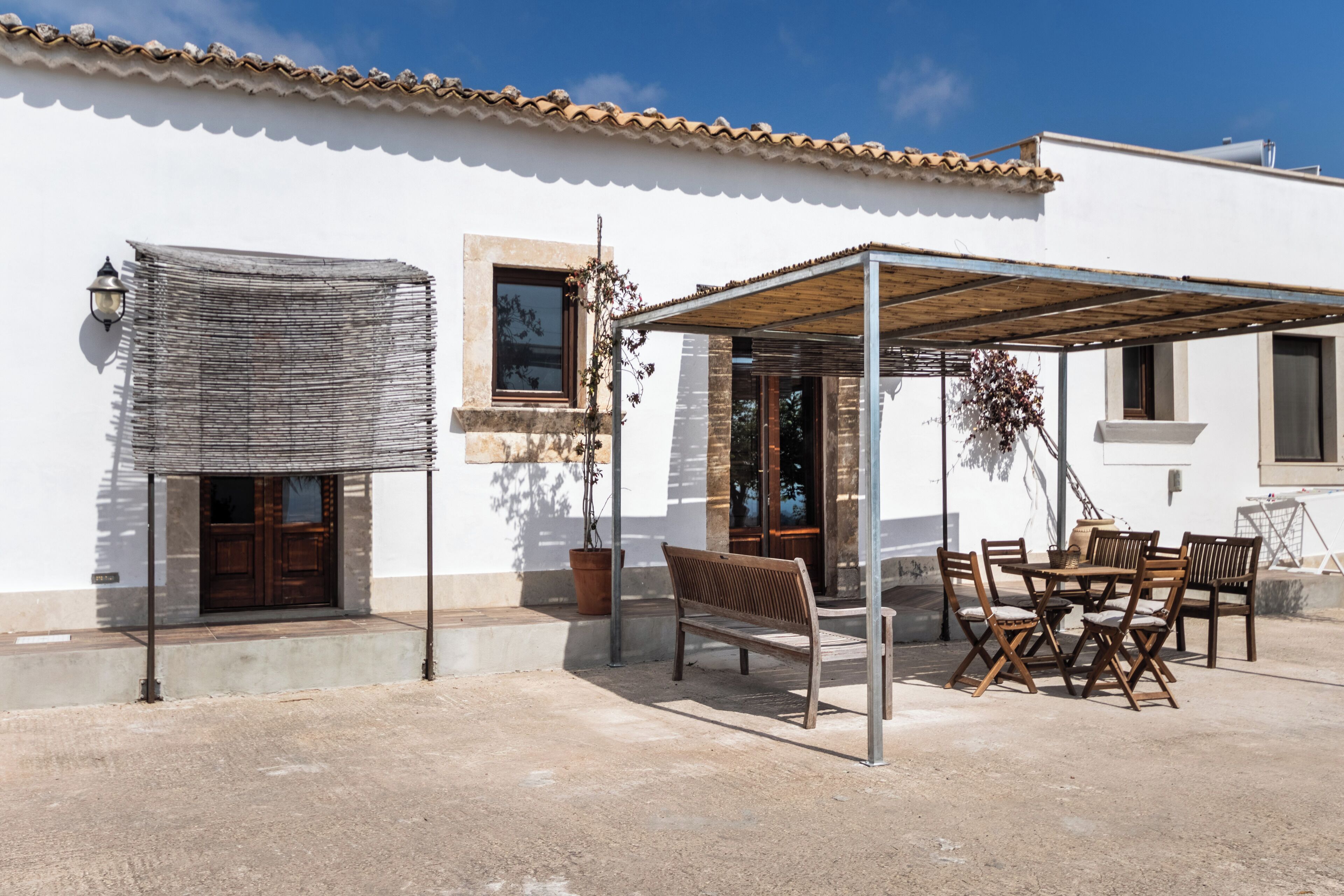 A patio with a wooden table and chairs, a bench, and a pergola.