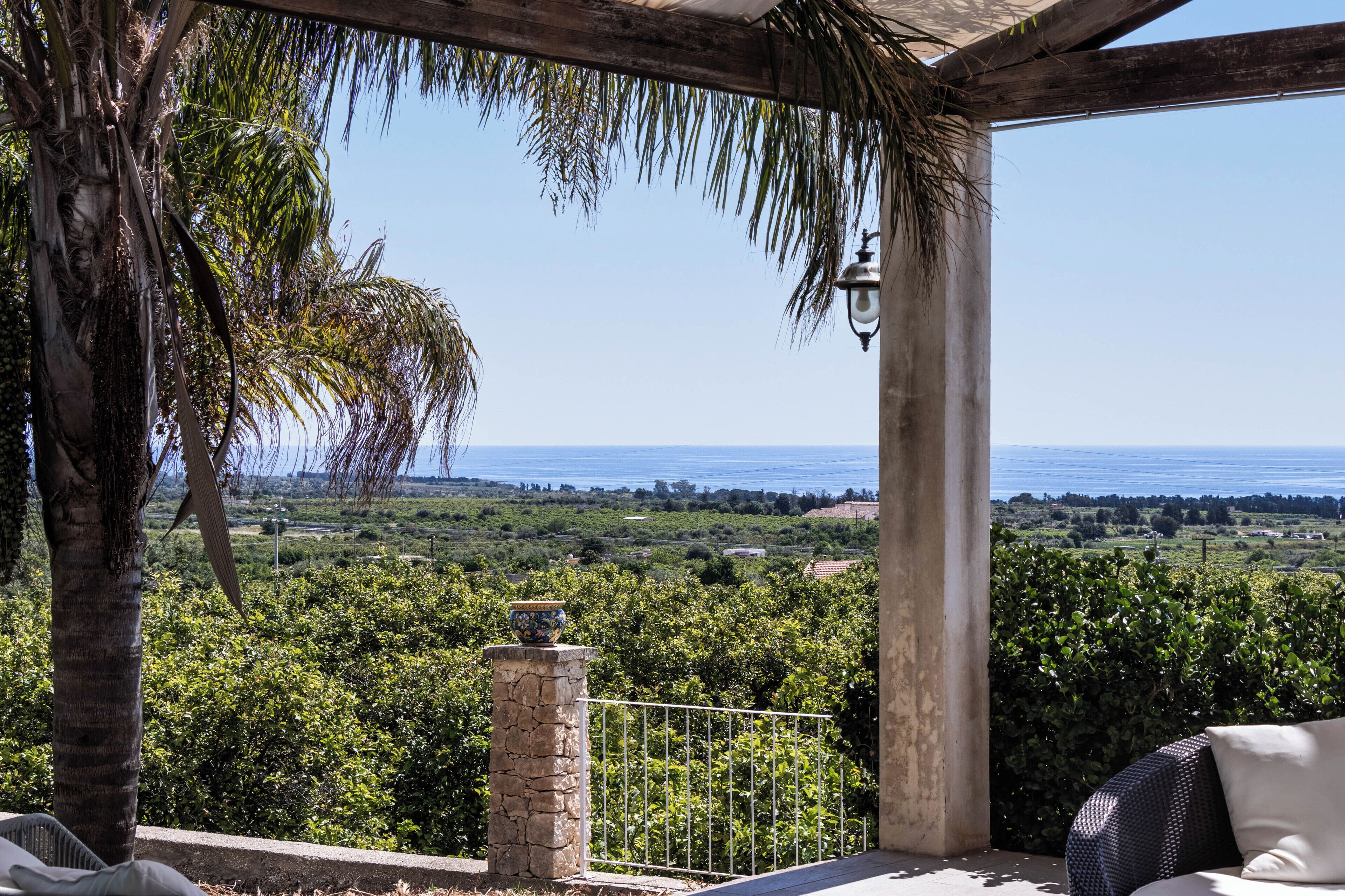 A covered outdoor seating area with a view of the sea and surrounding greenery.