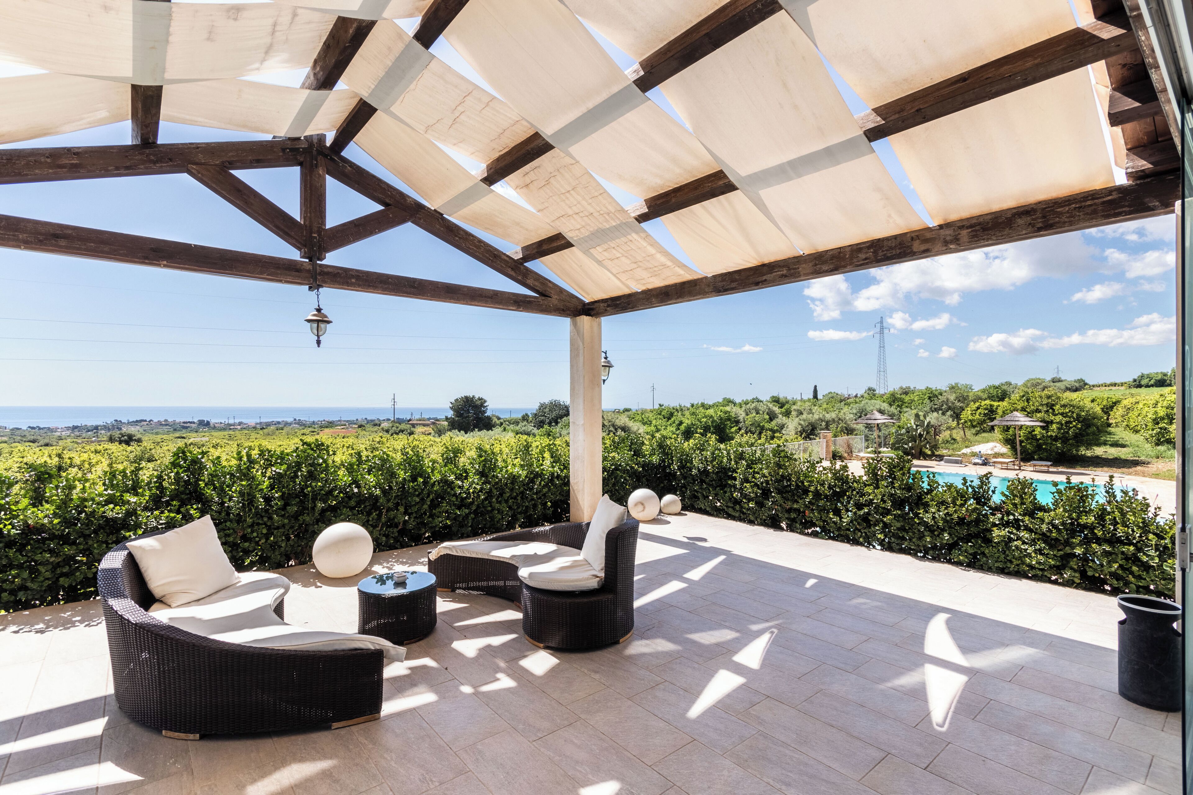 Un área de estar al aire libre techada con mobiliario de mimbre y vista al mar.