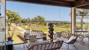 A covered outdoor seating area with wicker furniture, a table, and a bookshelf.