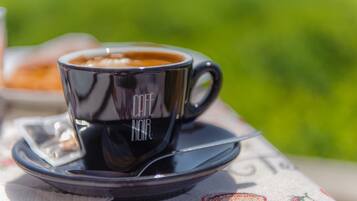 Una taza negra con el texto "CAFE NOIR" sobre un platito, colocada sobre una mesa con mantel estampado.