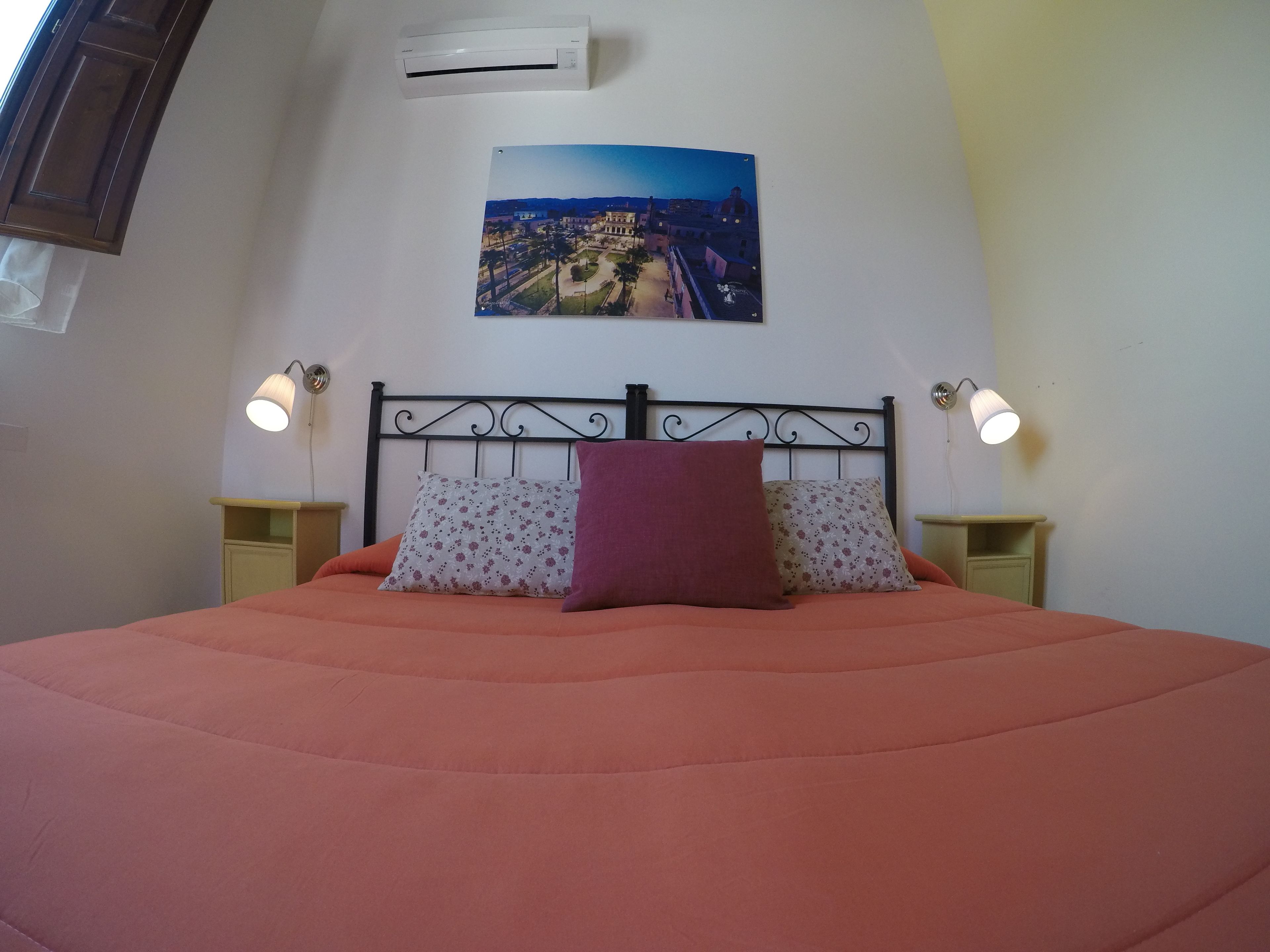 Een bed met hoofdeinde, twee nachtkastjes en een wandgemonteerde airconditioner.