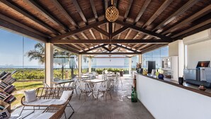 A covered outdoor area with seating, a kitchen area, and a view of the landscape.