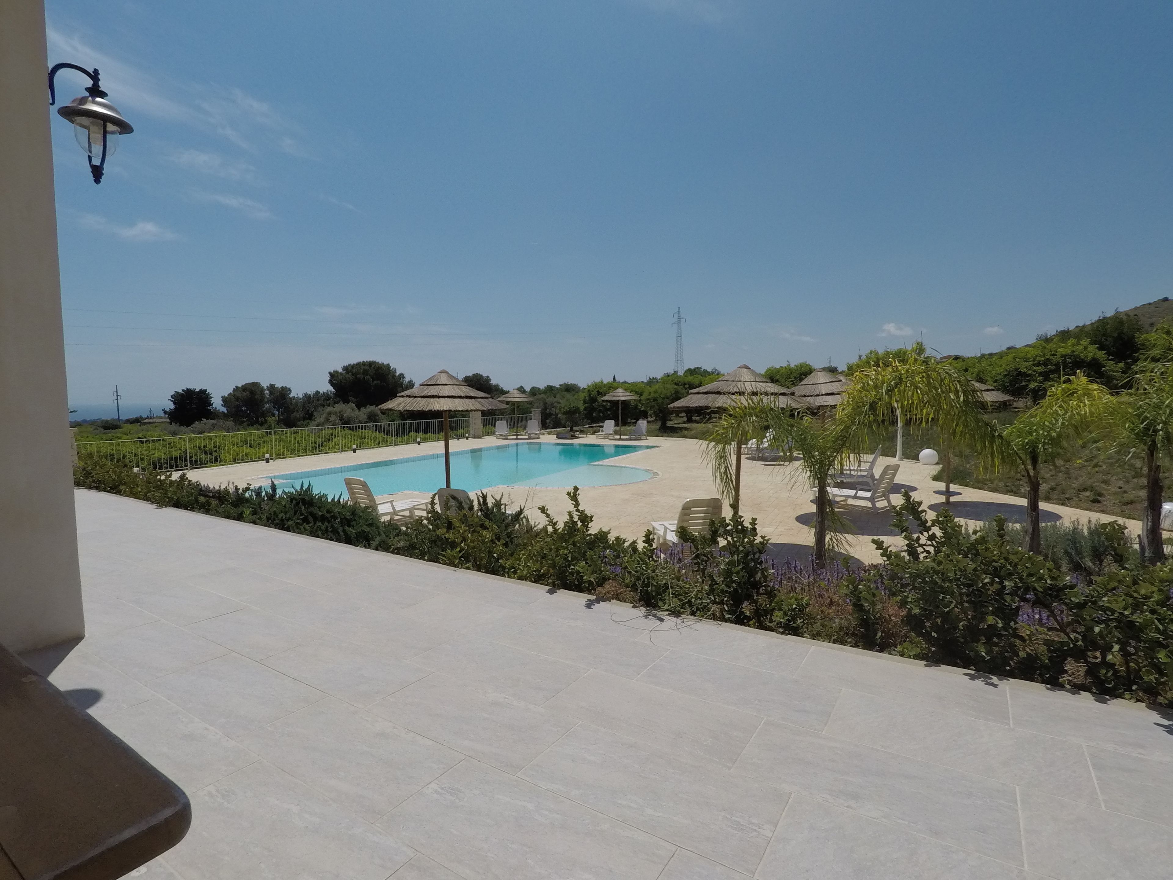 Una piscina amb gandules i ombrelles, envoltada de vegetació i un cel serè.