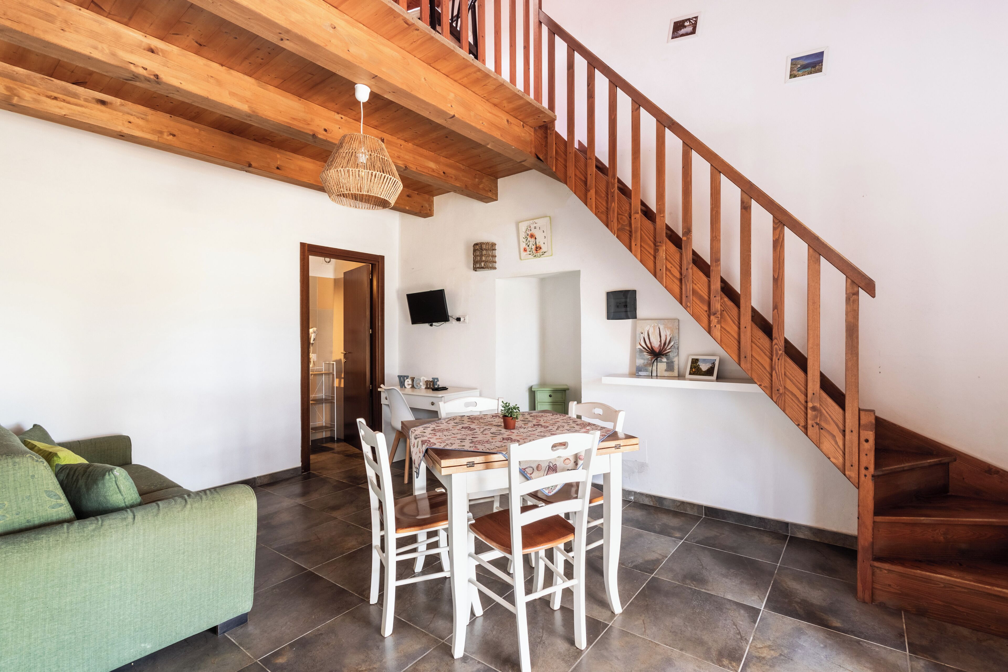 Ein Essbereich mit Holztisch, Stühlen und einer hängenden Leuchte. Eine Treppe mit Holzhandläufen führt zu einer oberen Ebene.