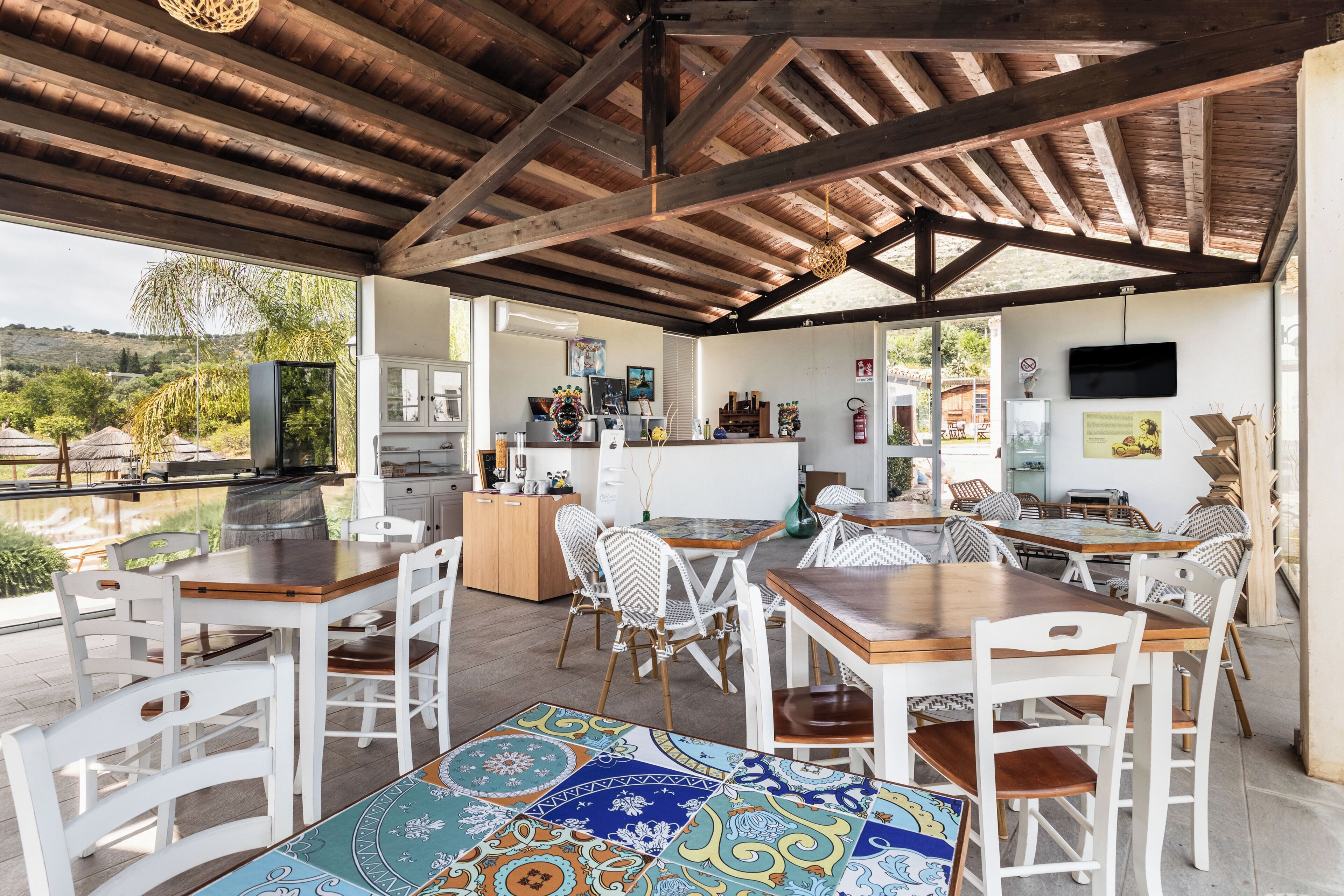 Un espace extérieur aménagé pour les repas, avec des tables et des chaises en bois, un coin cuisine doté de meubles blancs et une vue sur le paysage environnant.