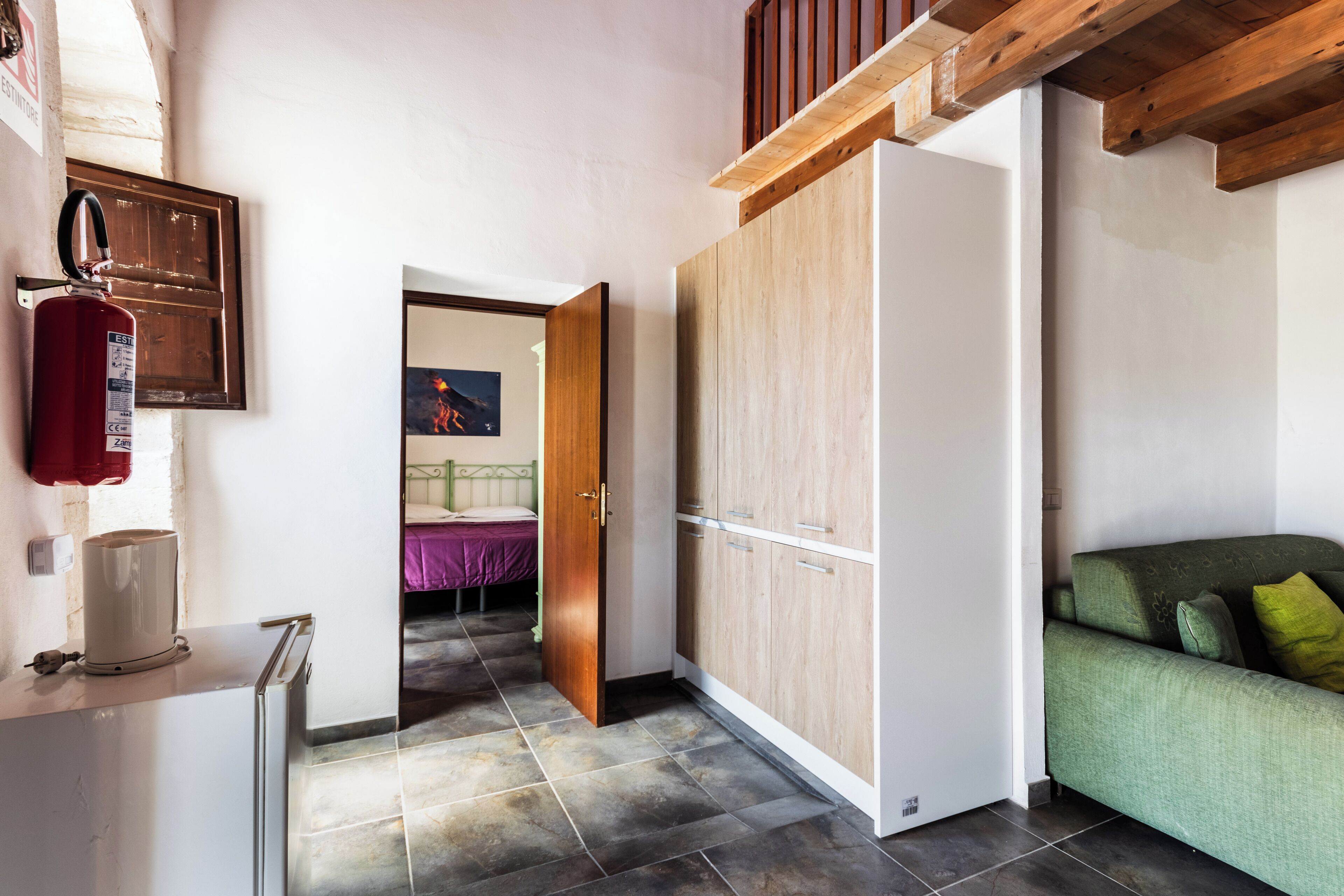 A room with a wooden ceiling, a green sofa, a white cabinet, and a door leading to another room.