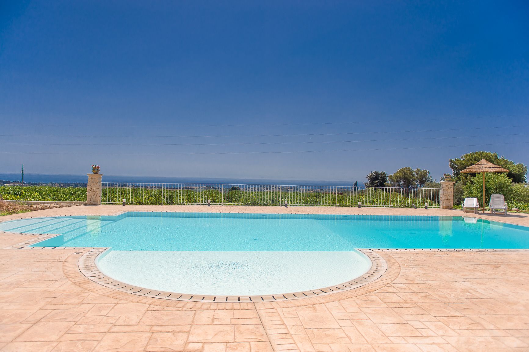 Une piscine offrant une vue dégagée sur la mer, entourée d’une terrasse dallée et d’une clôture.
