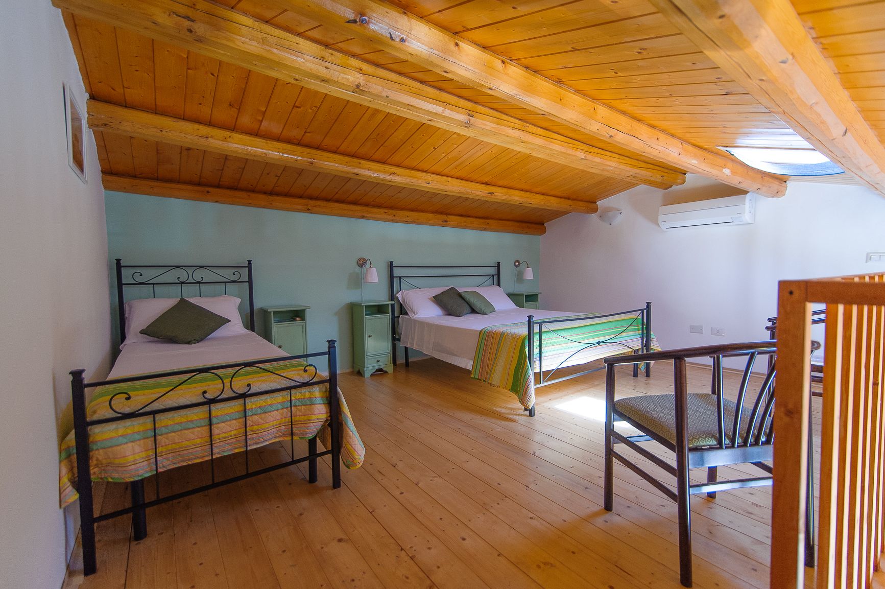 A bedroom with two beds, wooden flooring, and a sloped ceiling with exposed beams.