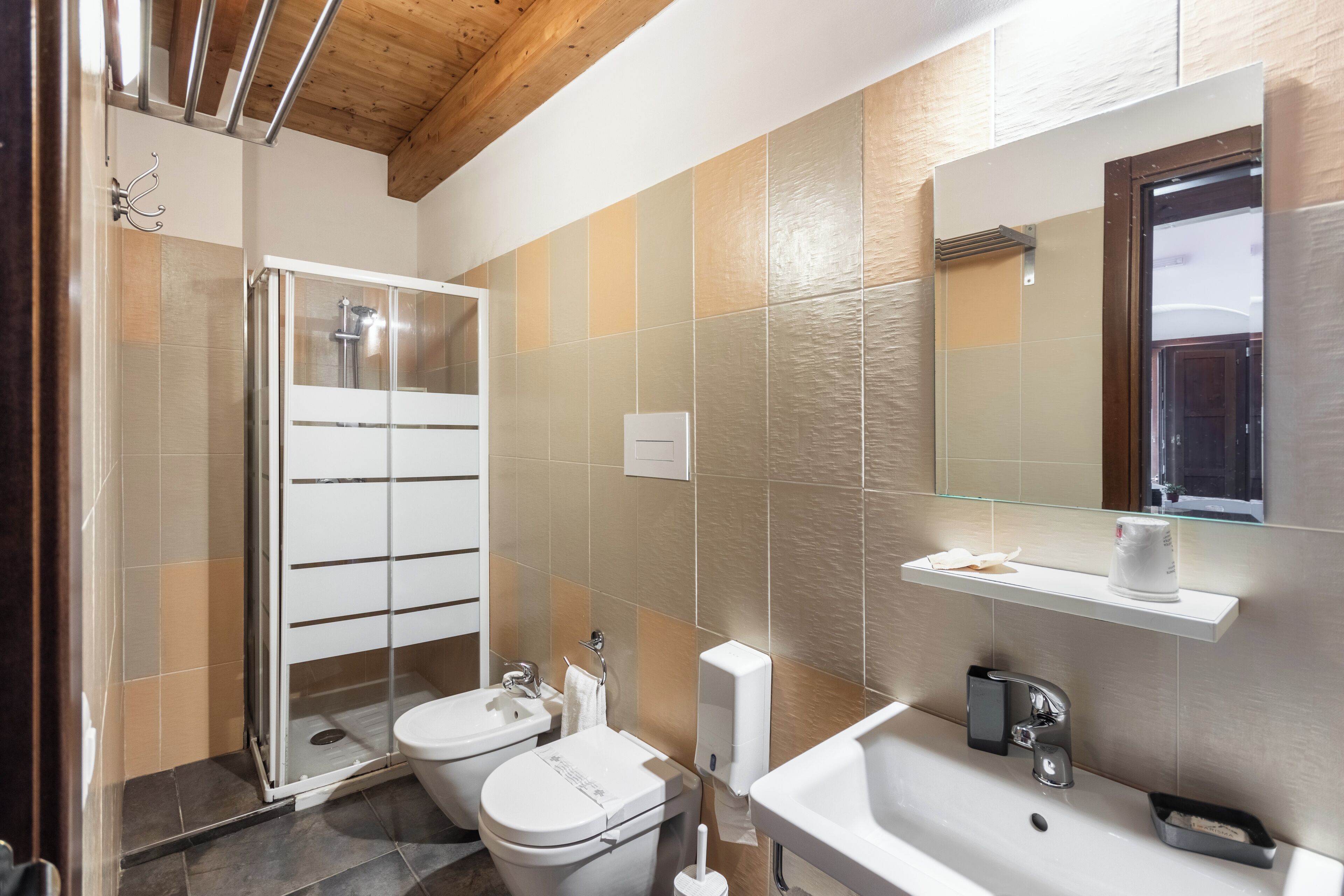 A modern bathroom with a glass shower enclosure, two toilets, a sink, and a mirror.
