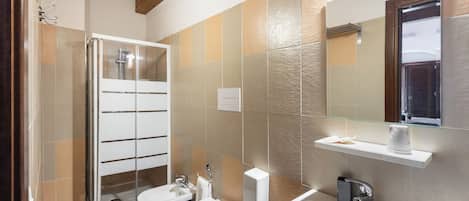 A modern bathroom with a glass shower enclosure, two toilets, a sink, and a mirror.