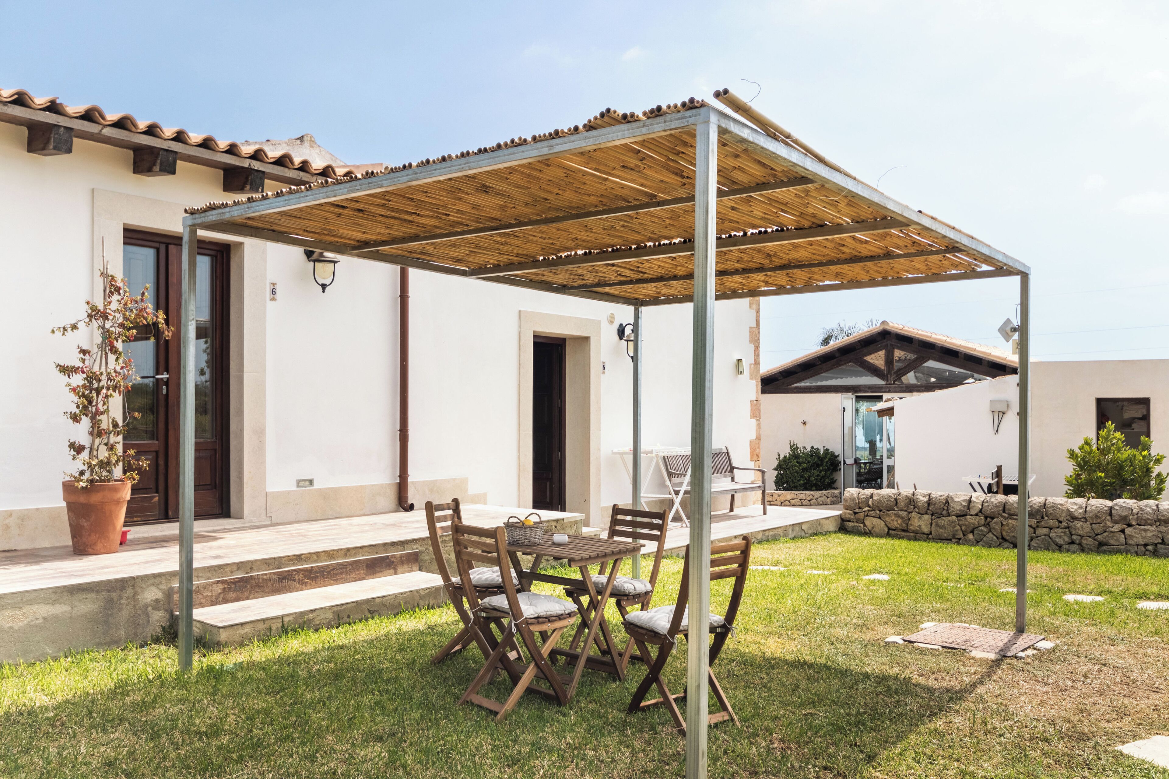 Une terrasse couverte avec une table et des chaises, une plante en pot et un mur de pierre.