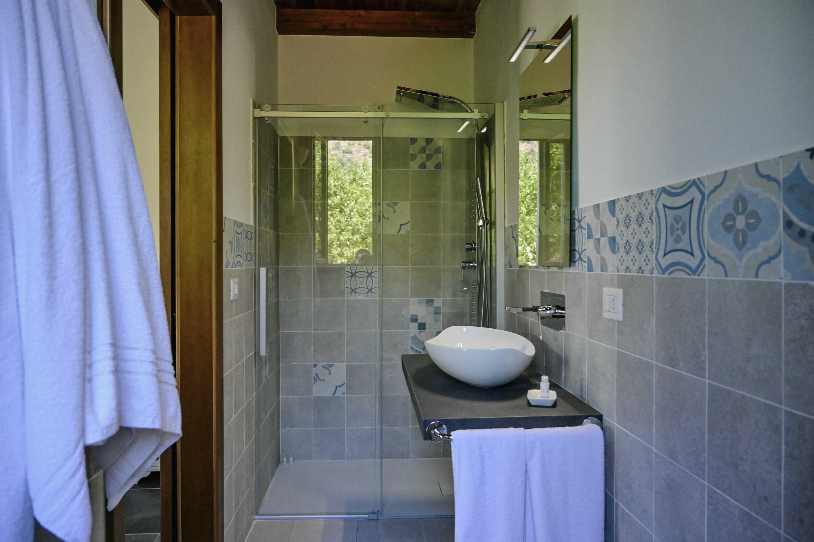 A modern bathroom with a glass-enclosed shower, a white sink, and patterned tiles.