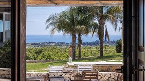 An outdoor patio with a view of the sea, stone walls, and wooden furniture.