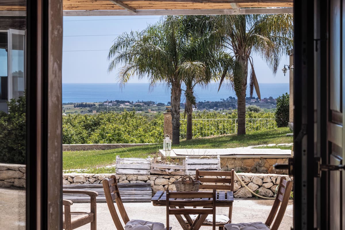 Eine Terrasse im Freien mit Blick auf das Meer, Steinmauern und Holzmöbeln.