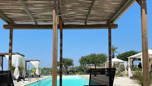 Un espacio exterior techado con piscina, sillas de descanso y sombrillas.