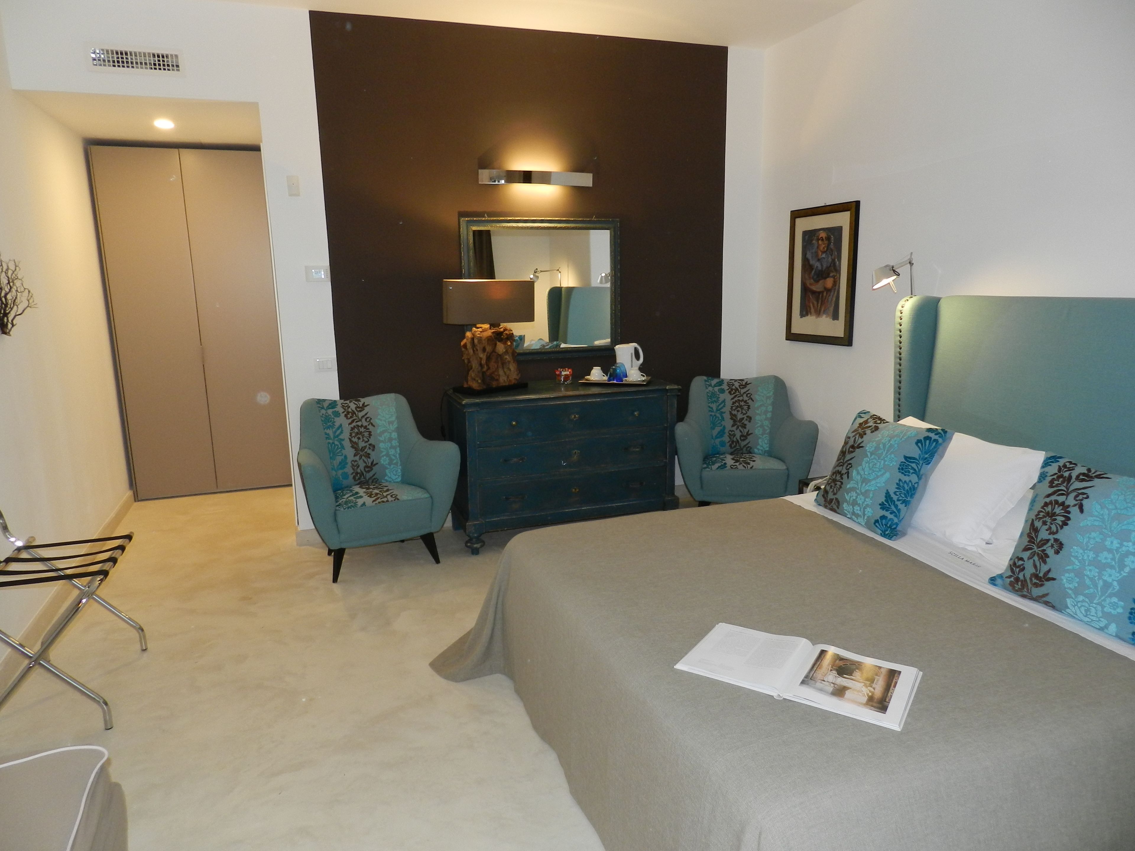 A bedroom with a bed, two armchairs, a dresser, a mirror, and a door.