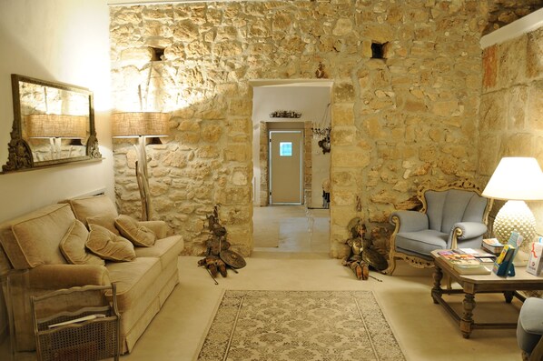 A cozy living room with a stone wall, a sofa, a chair, a coffee table, and a lamp. - Scilla Maris Charming Suites-Restaurant (Noto)