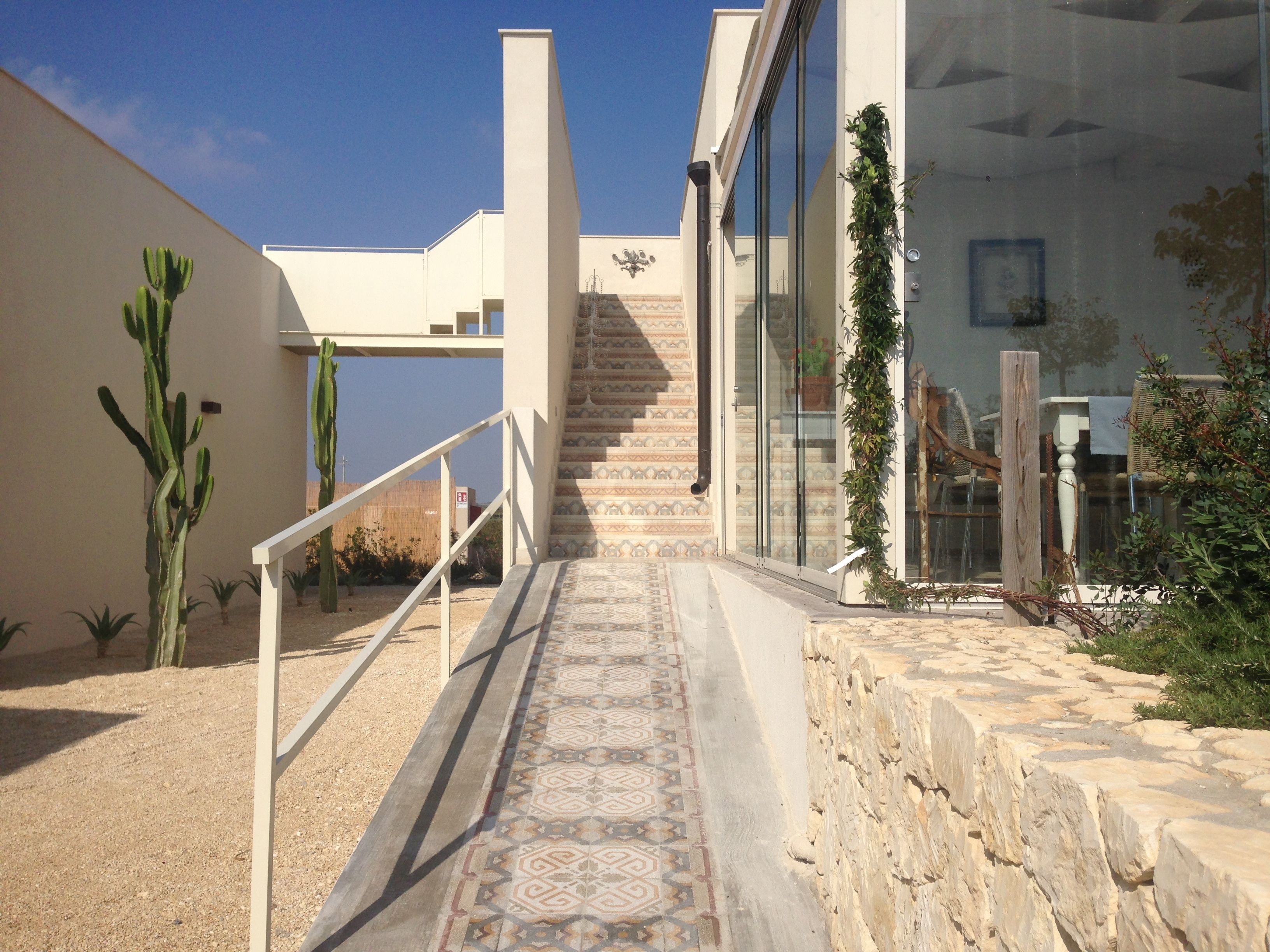 Un escalier menant à un bâtiment dont le sol est décoré de motifs, avec un cactus et une clôture en bois.