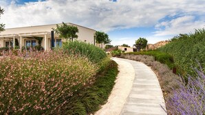 Un edificio con un corredor cubierto, rodeado de jardines ajardinados con diversas plantas y flores.