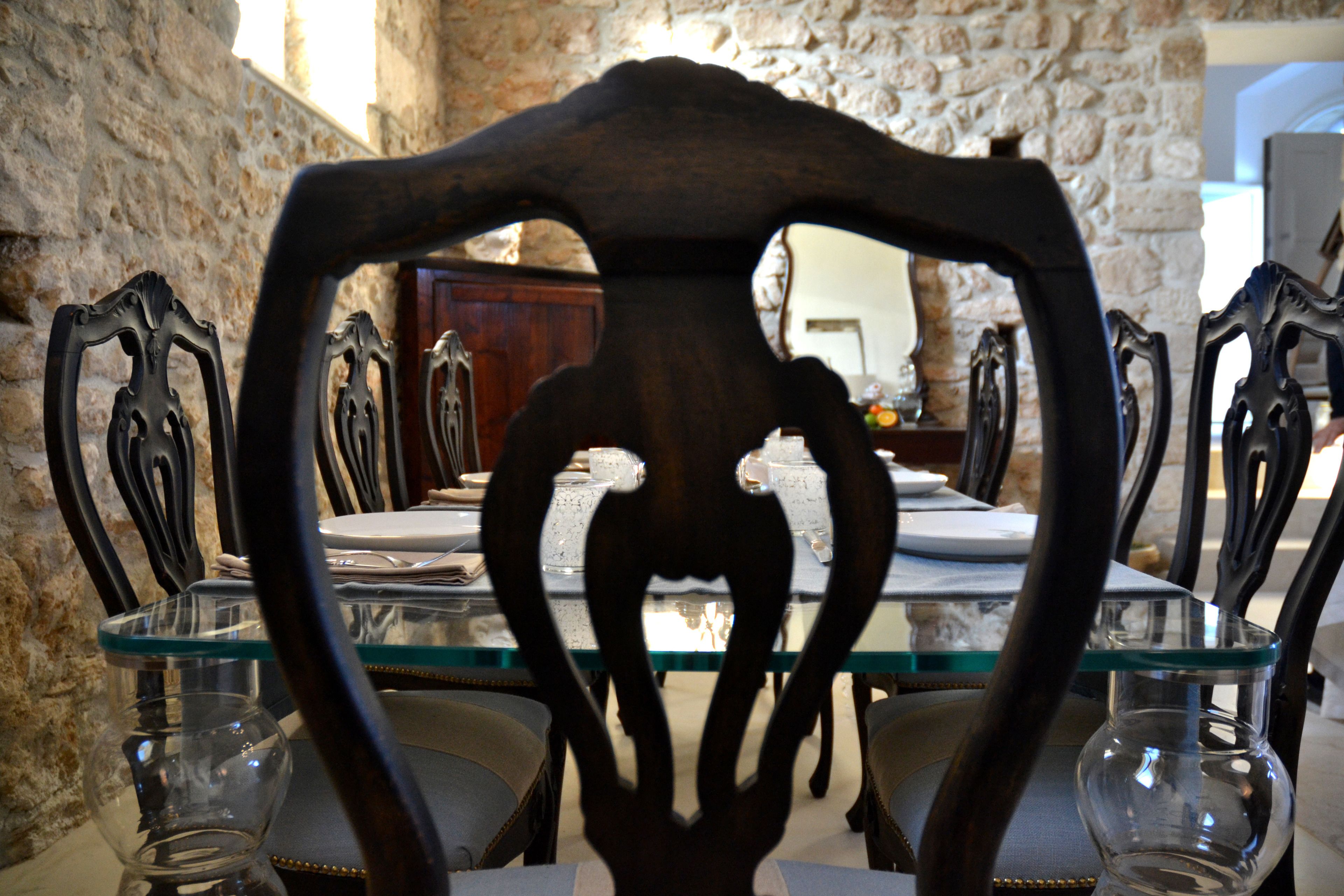 A dining table with chairs, a glass vase, and a stone wall in the background.