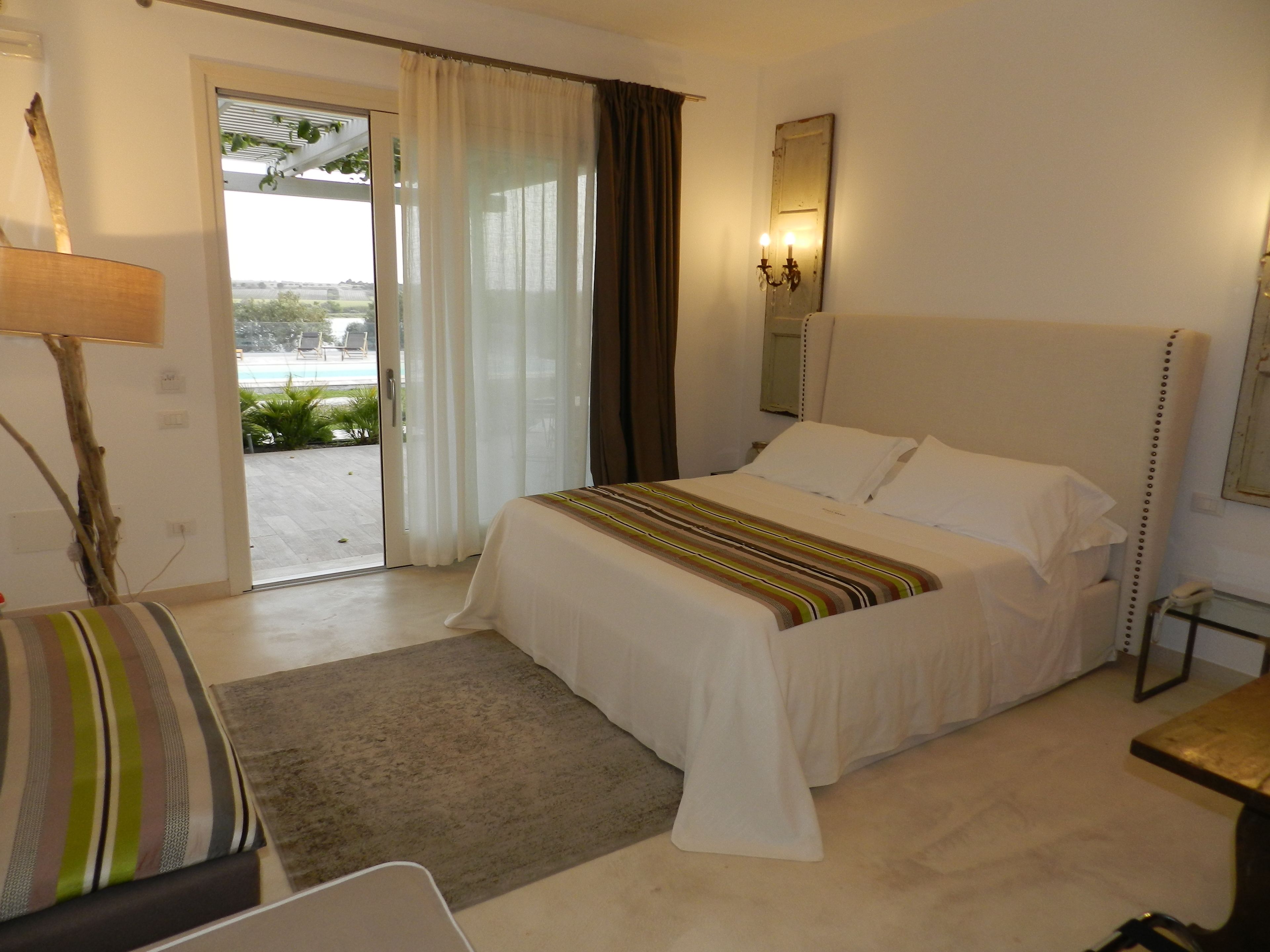 A hotel room with a bed, a desk, a lamp, and a view of the outdoors.