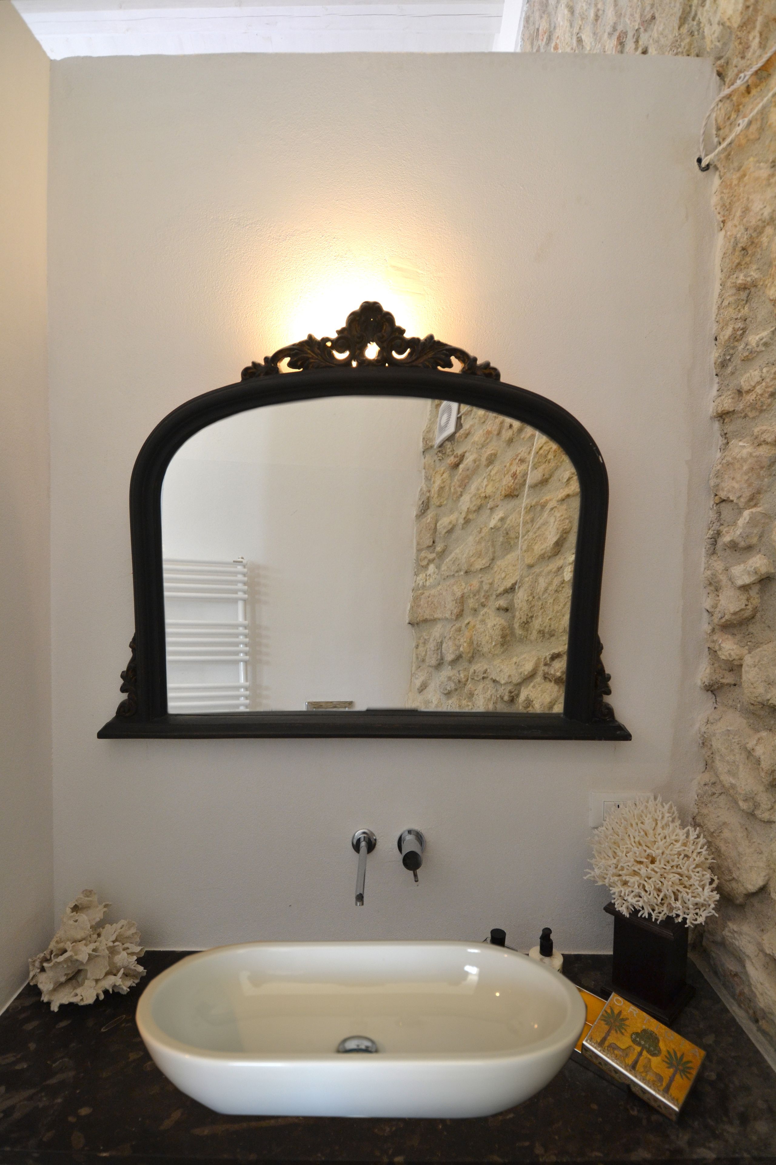 A bathroom with a white sink, a black ornate mirror, and a stone wall.