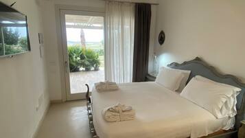 Habitación de hotel con una cama, televisor montado en la pared, ventana con cortinas y vista a zonas verdes.