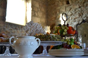 A table with a white teapot, a glass cup, a fruit platter, and a plate with a knife. - Scilla Maris Charming Suites-Restaurant (Noto)