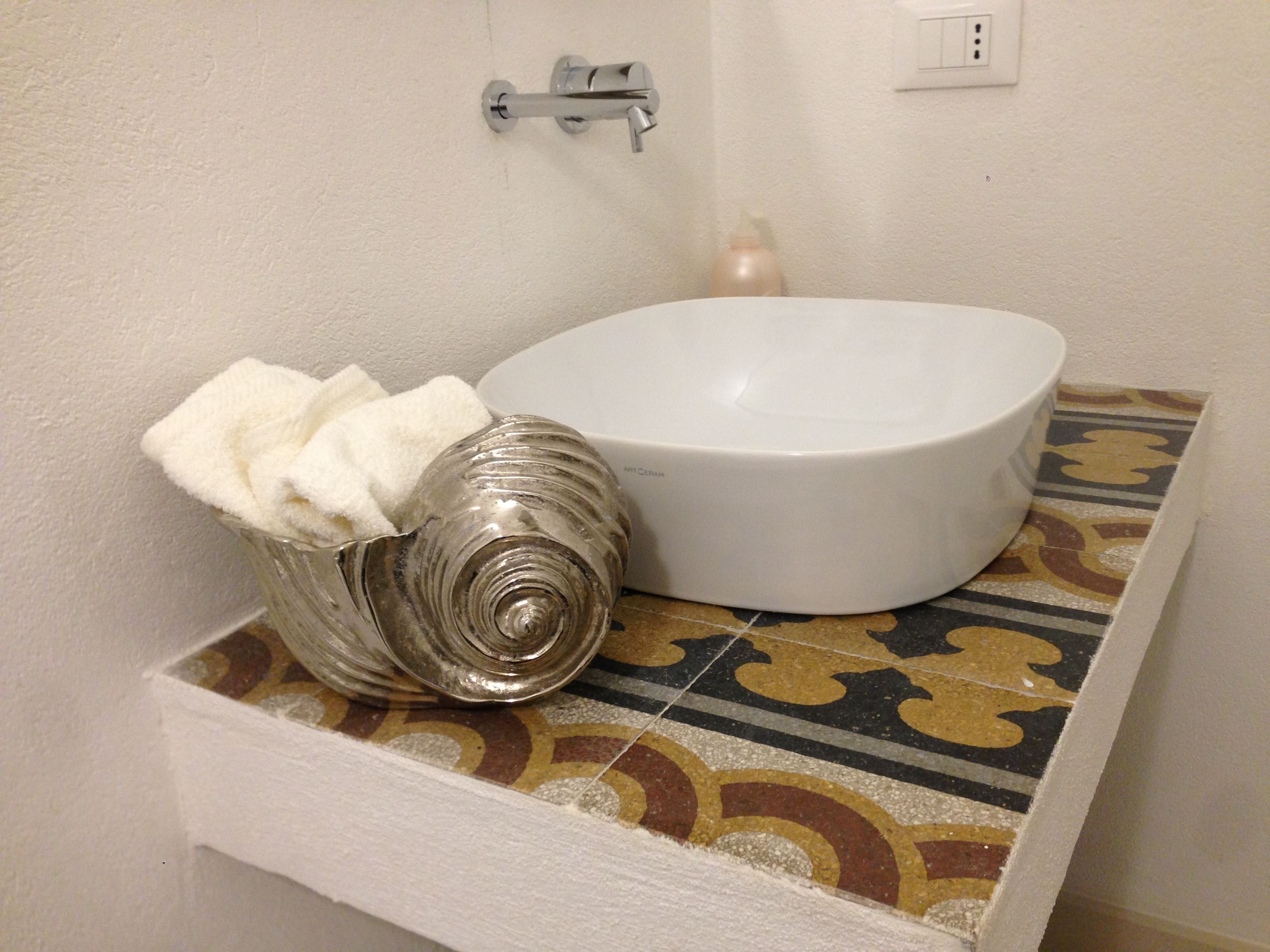 A bathroom with a white ceramic sink, a decorative shell, and a patterned tile backsplash.